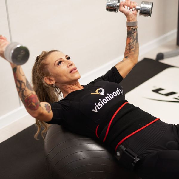 Žena cvičiaca s činkami v oboch rukách na fitness lopte.