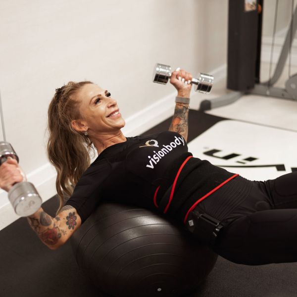 Žena cvičiaca s činkami v oboch rukách na fitness lopte.